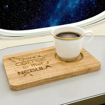 A Voyager Breakfast Board displays the engraved phrase "There's Coffee in that Nebula" while holding a full cup of coffee against a backdrop of stars and a spaceship window.