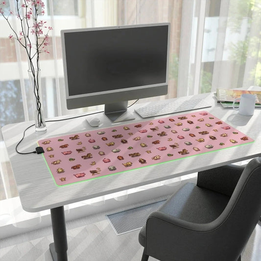 A pink Stardew Valley desk mat featuring pixel art of animals sits on a wooden desk next to a computer monitor and office supplies.