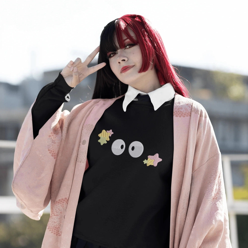 A person wearing a black Soot Sprites embroidered hoodie stands outside raising one hand while making a peace sign.