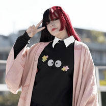 A person wearing a black Soot Sprites embroidered hoodie stands outside raising one hand while making a peace sign.