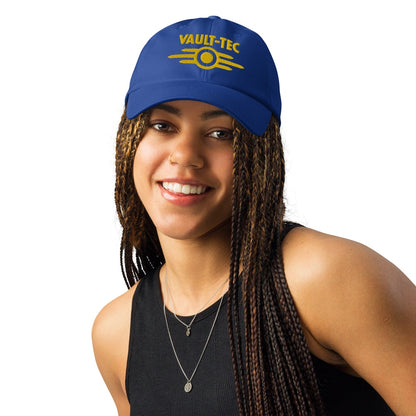 A person wears a blue Vault-Tec baseball cap with yellow embroidered lettering and logo, referencing the Fallout video game series.