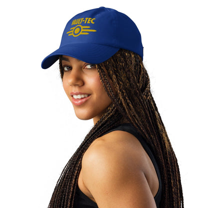 A person wears a blue Vault-Tec baseball cap with yellow embroidered lettering referencing the Fallout video game series.