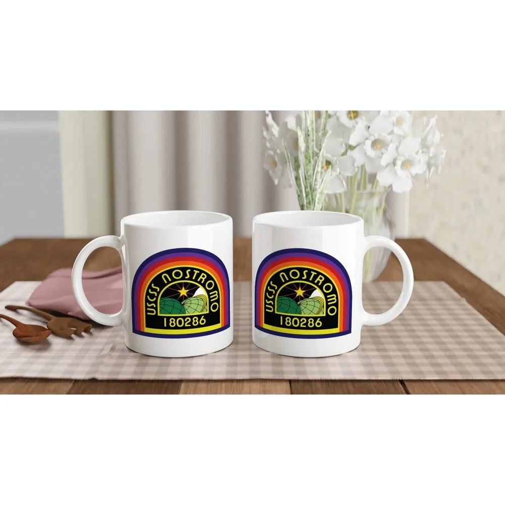 Two white ceramic mugs display a rainbow-colored USCSS Nostromo logo and number 180286.