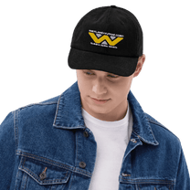 A person wearing a black baseball cap embroidered with the Weyland-Yutani Corp logo from Alien.