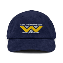 A navy blue baseball cap features an embroidered Weyland-Yutani Corp logo and the phrase "Building Better Worlds.