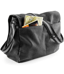 A dark grey canvas messenger bag featuring a pocket containing papers and an adjustable shoulder strap.