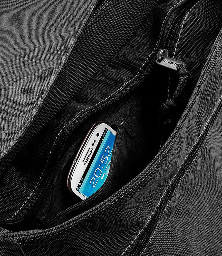 A smartphone is tucked into a zippered pocket of a black canvas messenger bag.