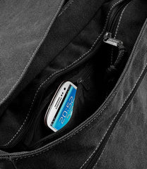 A smartphone is tucked into a zippered pocket of a black canvas messenger bag.