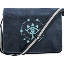 A navy blue Zelda Sheikah messenger bag features glow-in-the-dark embroidery of a stylized eye symbol on the front flap.